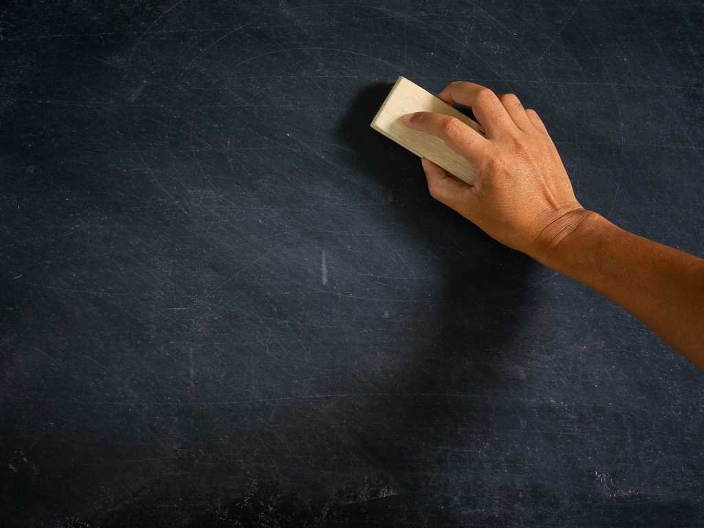 A hand holds an eraser erasing a blackboard.