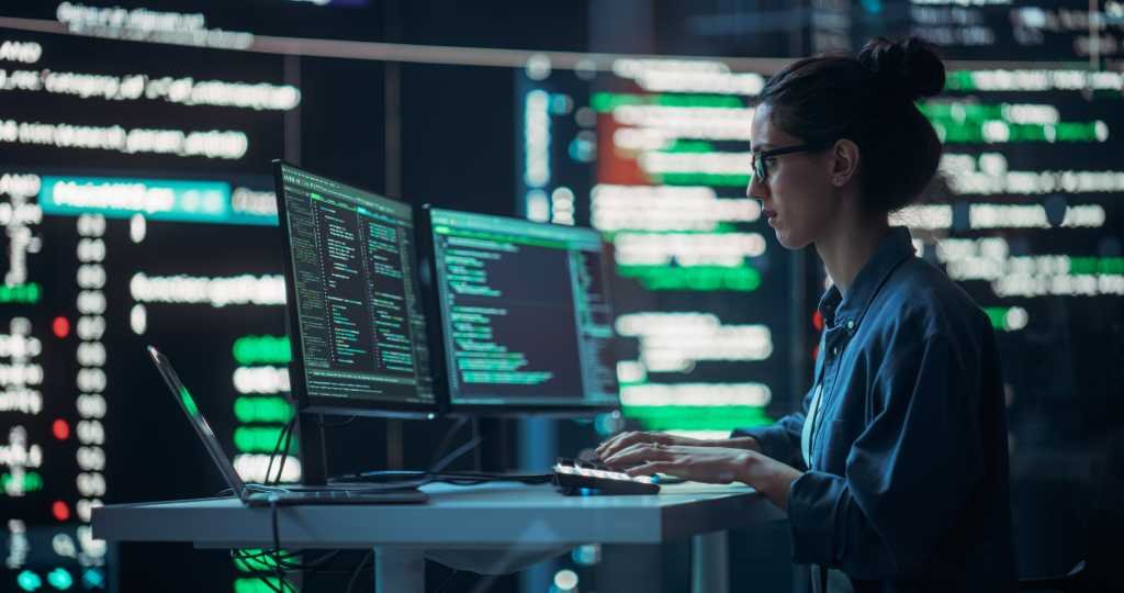 Female Developer Thinking and Typing on Computer, Surrounded by Big Screens Showing Coding Language. Professional Programmer Working in an Office, Running Coding Tests. Futuristic Programming