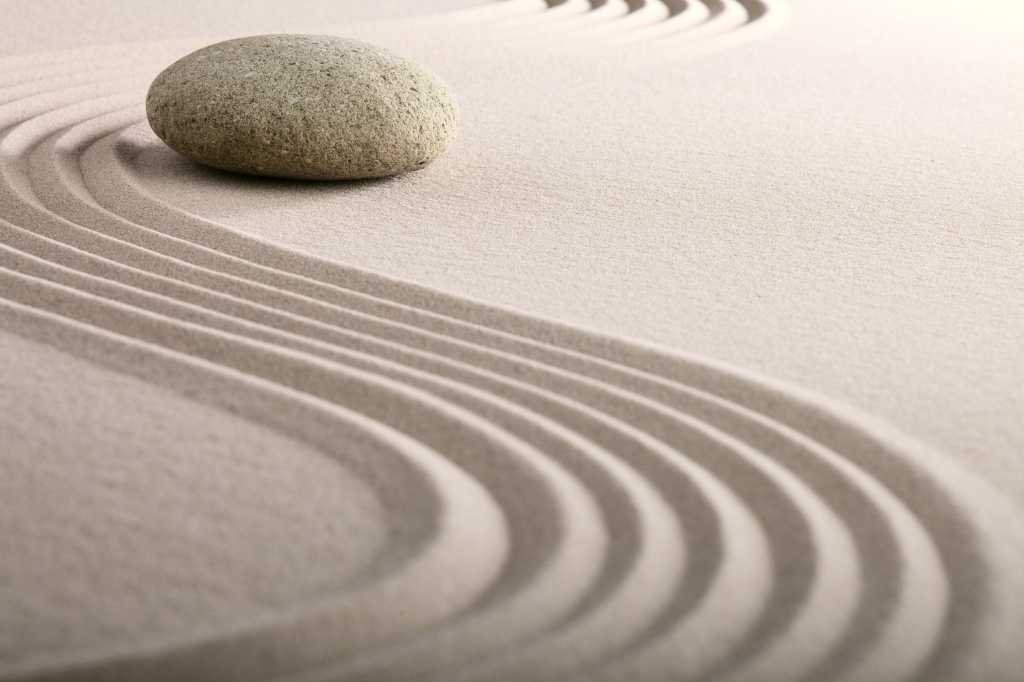 Parallel lines in the sand curving around a rock ; zen stone garden round stone and raked sand